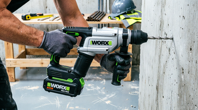 Worker wearing gloves using WORX rotary hammer drill on concrete wall in workshop