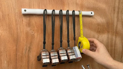 A finished DIY PVC pipe tape measure holder mounted on a wooden wall, neatly organizing a row of clean measuring tapes hanging by their wrist straps | HomeDIYer